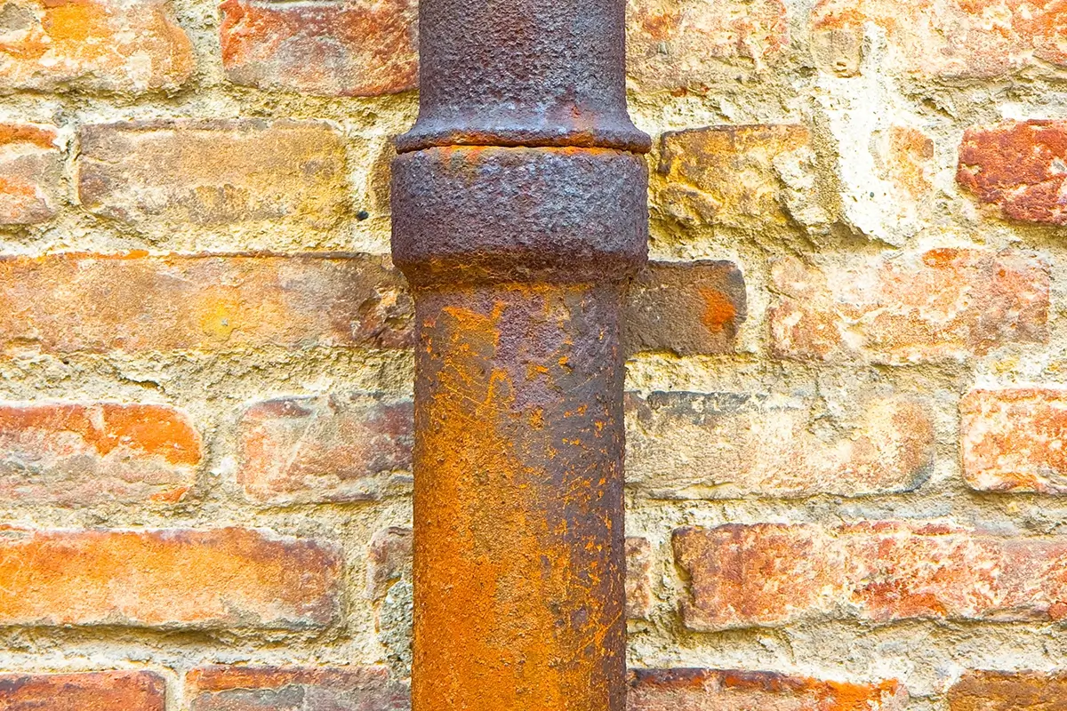 Rust on exterior pipe in front of a brick wall.