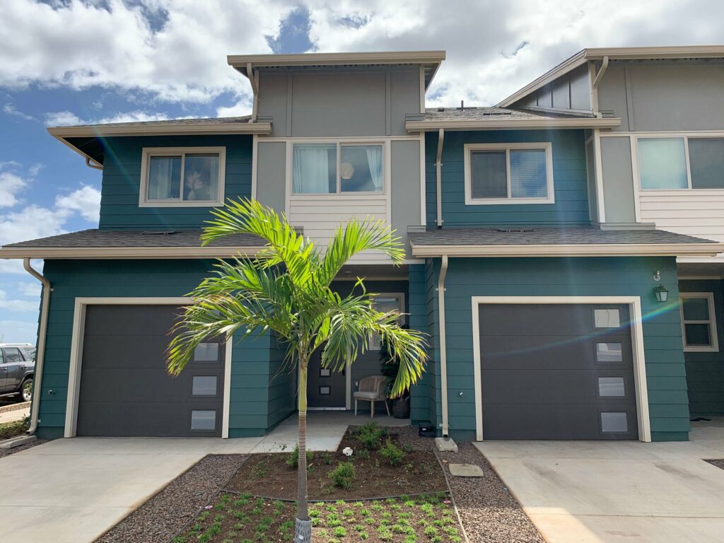 A blue and white townhouse with a palm tree and driveway in front of it
