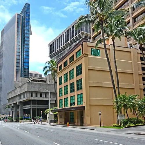 There are a series of commercial buildings in front of a street with people walking around