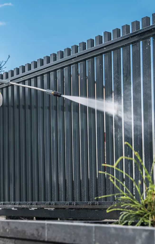 Someone is power washing a metal fence with a hose