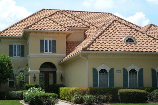 A large yellow three story house with a clean brown roof after a power washing. There are neatly trimmed bushes in front of the house and a number of large windows.