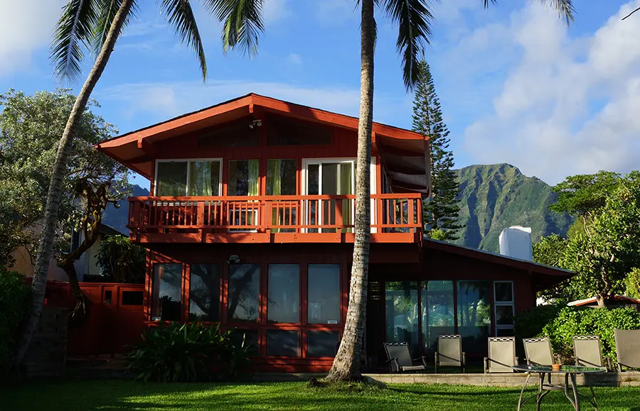 Red two story beach house with tall coconut trees in Hawaii