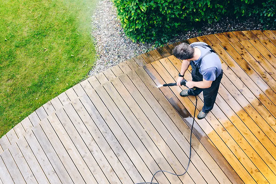 man cleaning terrace with a power washer - high water pressure cleaner on wooden terrace surface