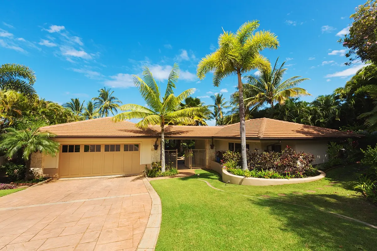 Hawaiian home with palm trees outside and behind the house. A clean, manicured yard and driveway out front.